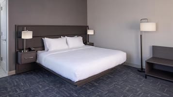 A neatly made hotel room with a large bed, two bedside tables with lamps, a nightstand, and a bench.