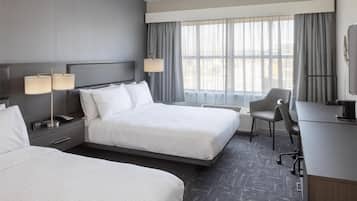 Habitación de hotel con dos camas, un escritorio, una silla, un televisor y una ventana con cortinas.