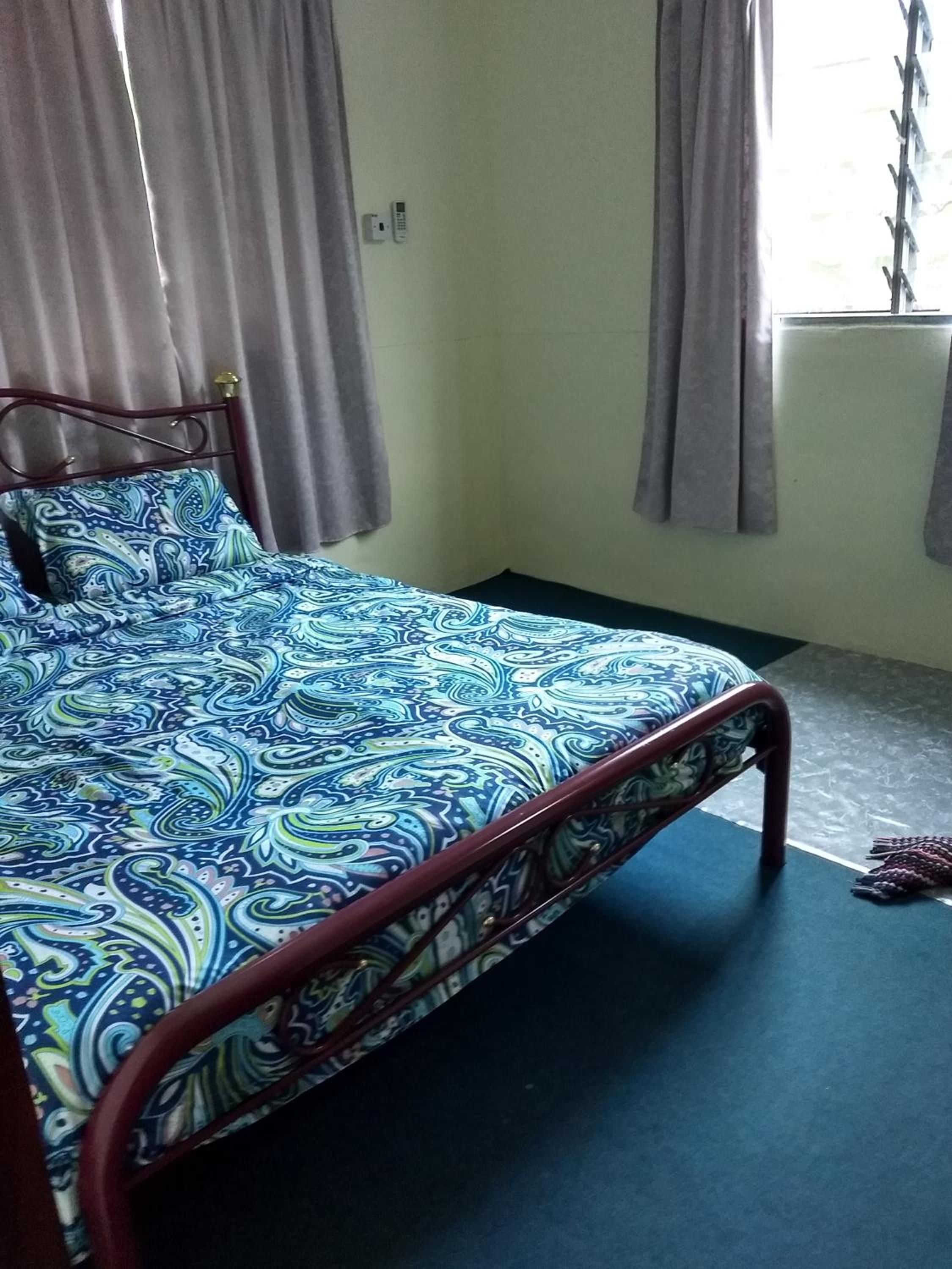 Una cama con una colcha estampada, estructura metálica y cortinas en una ventana.