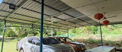 A covered outdoor area with a car parked under a metal roof, a table, and red lanterns.