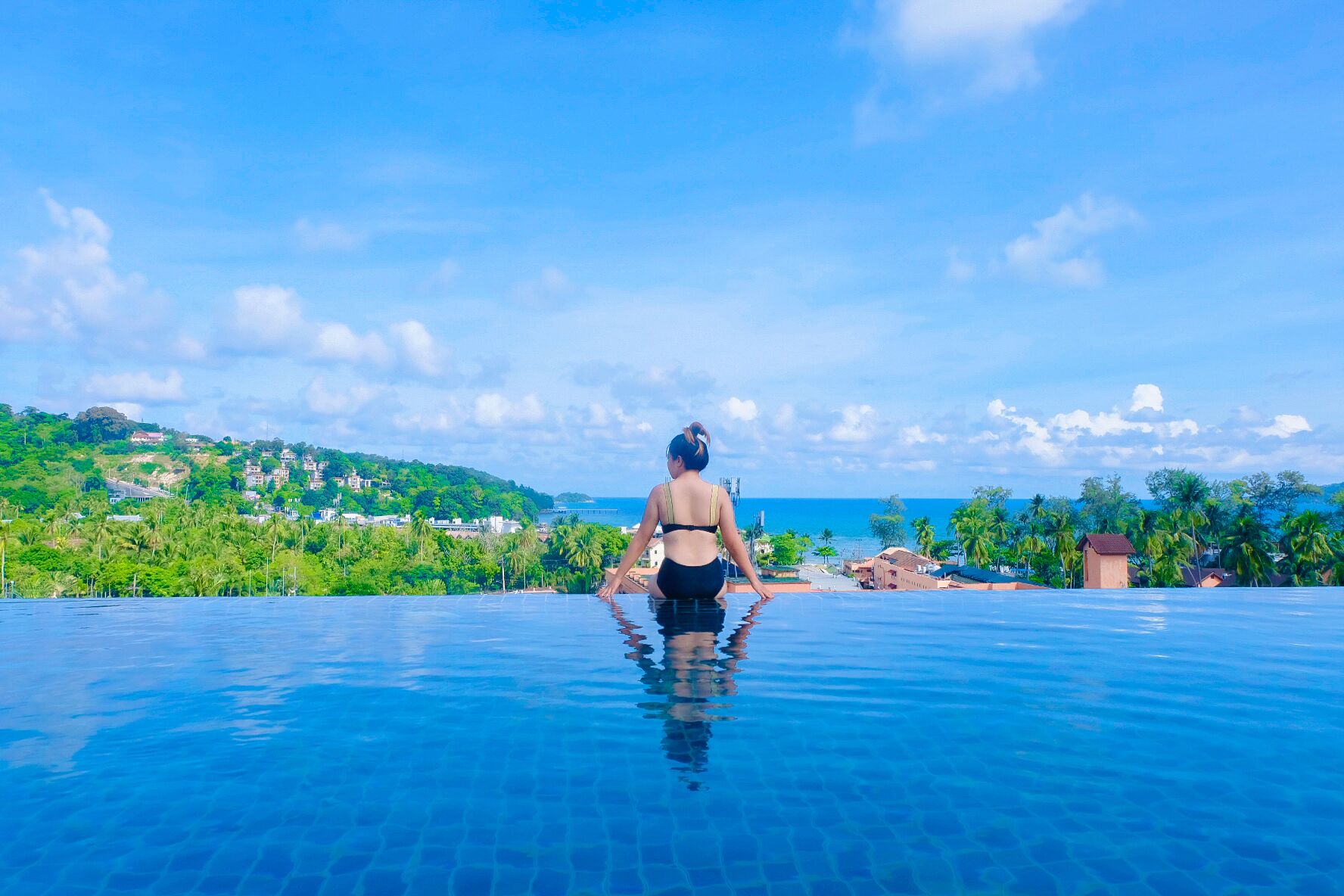Eine Person entspannt sich an einem Infinity-Pool mit Blick auf den Ozean und eine grüne Landschaft.