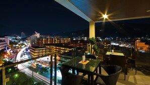 A rooftop terrace with glass railings, tables, and chairs, overlooking a cityscape at night. - YouDee Hotel Patong (formerly Meir Jarr Hotel) (Patong)