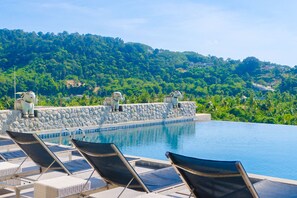 Una piscina con sillas de descanso y estatuas de piedra en una terraza con vistas a una ladera verde y exuberante.