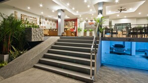 A modern hotel lobby with a staircase, reception desk, and a view of the parking area. - YouDee Hotel Patong (formerly Meir Jarr Hotel) (Patong)
