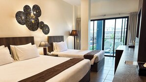 A hotel room with two beds, a large window with a view of the city, a desk, and a decorative wall piece. - YouDee Hotel Patong (formerly Meir Jarr Hotel) (Patong)