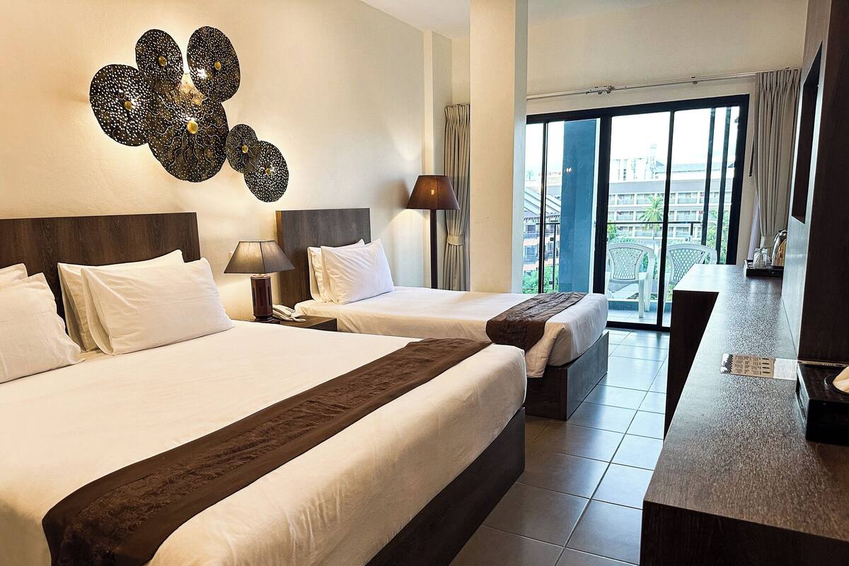 A hotel room with two beds, a large window with a view of the city, a desk, and a decorative wall piece.