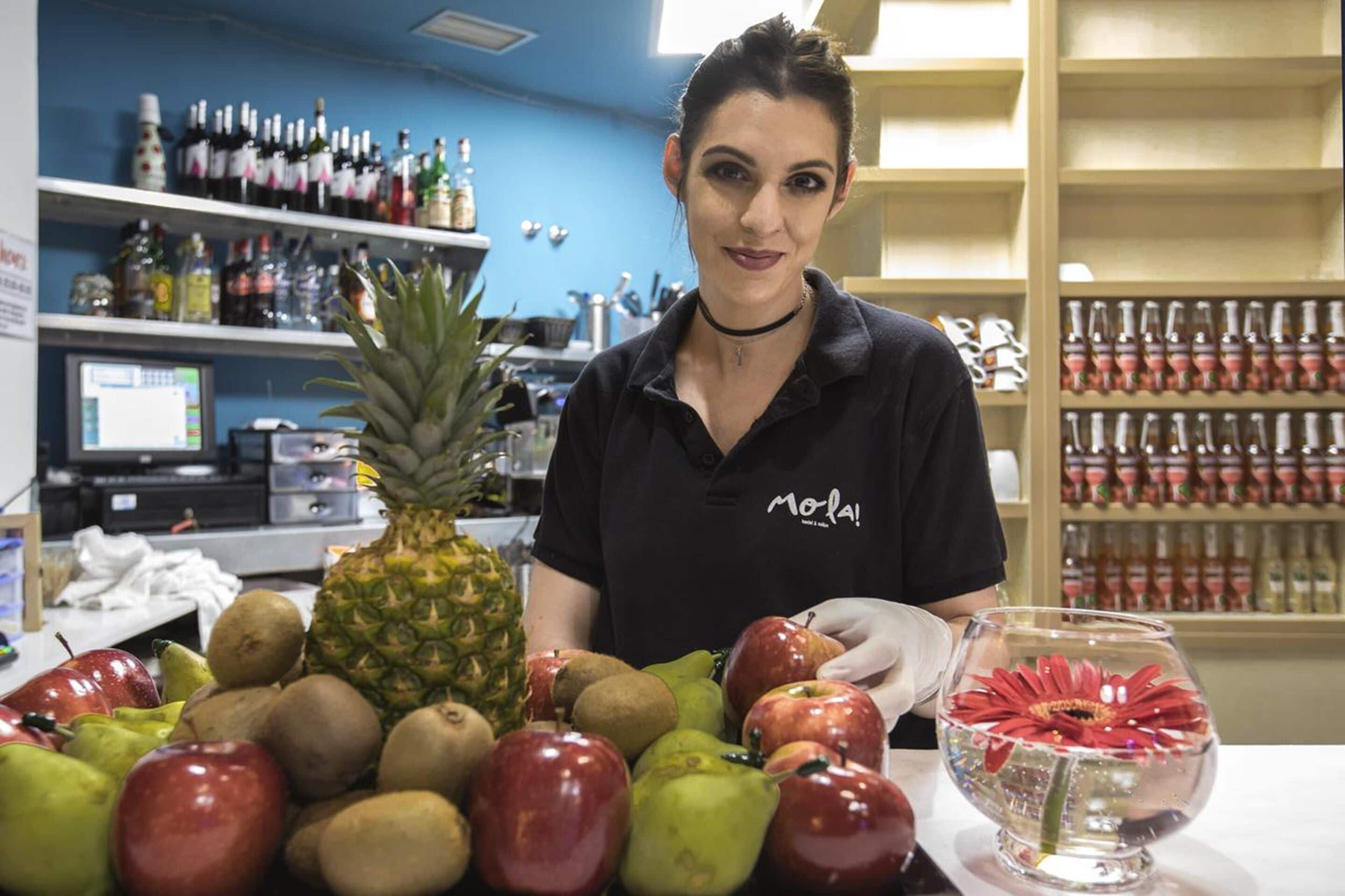 Iemand staat achter een tafel met verschillende soorten fruit en een vissenkom.