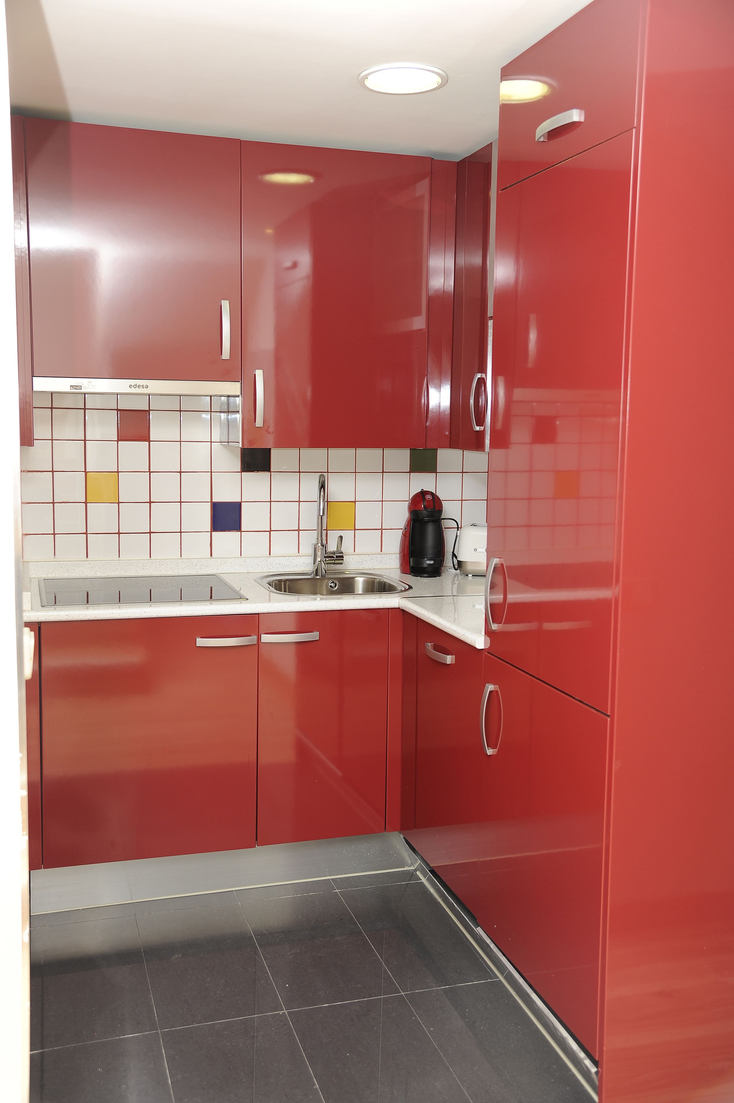 Een keuken met rode kastjes, een wit aanrechtblad en een zwart betegelde spatwand.