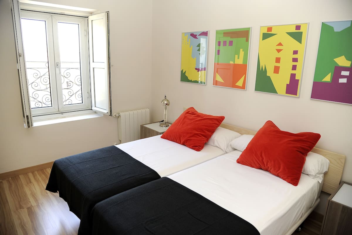 A double bed with red and white bedding, a nightstand with a lamp, and a window with decorative ironwork.