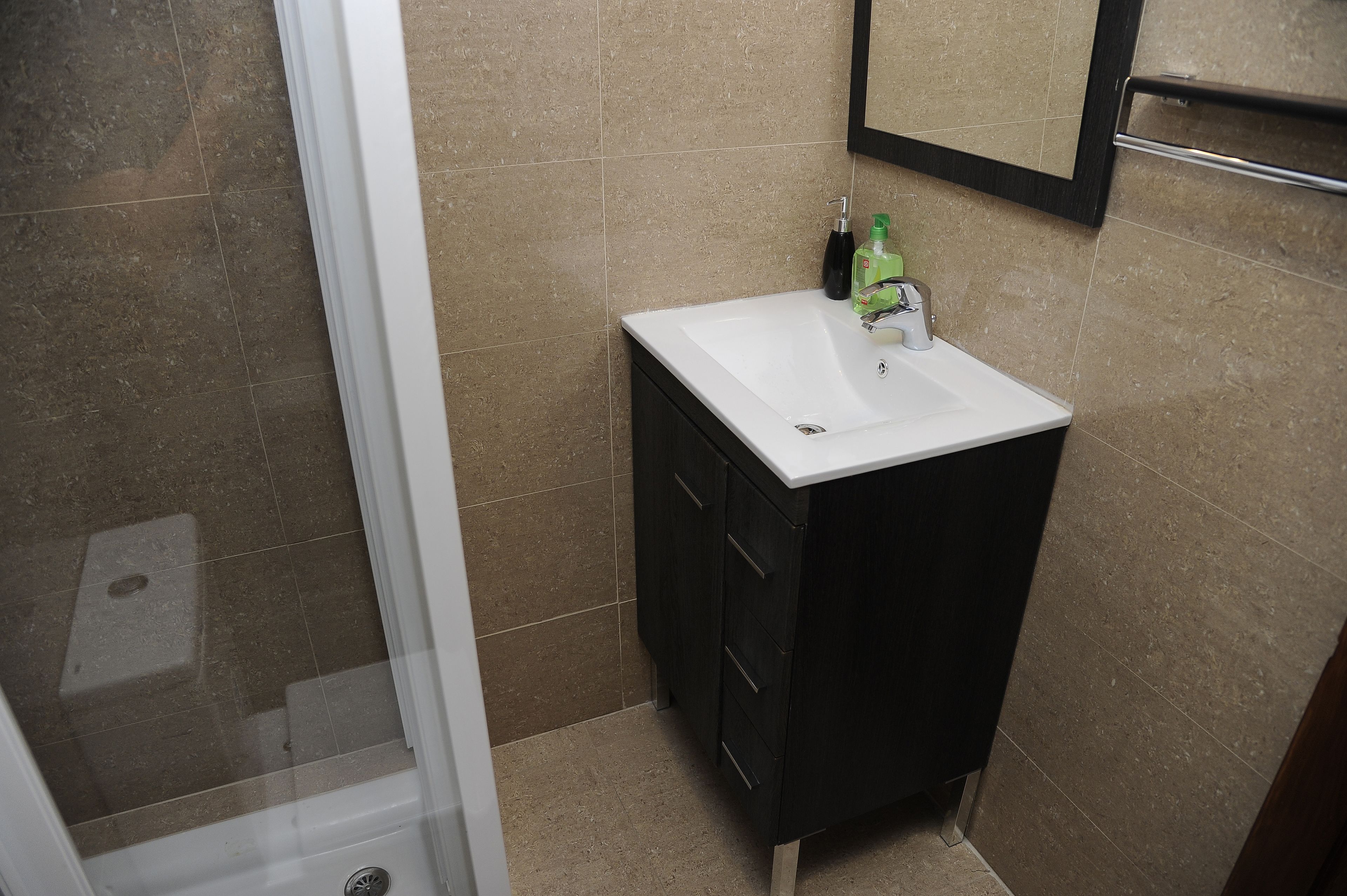 Un baño con un lavamanos blanco, un mueble oscuro y un espejo encima.