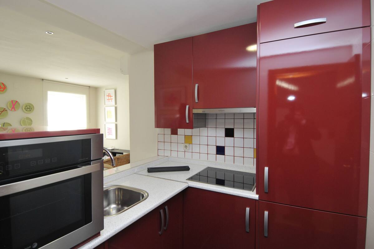 A kitchen with red cabinets, a stainless steel sink, and a tiled backsplash.