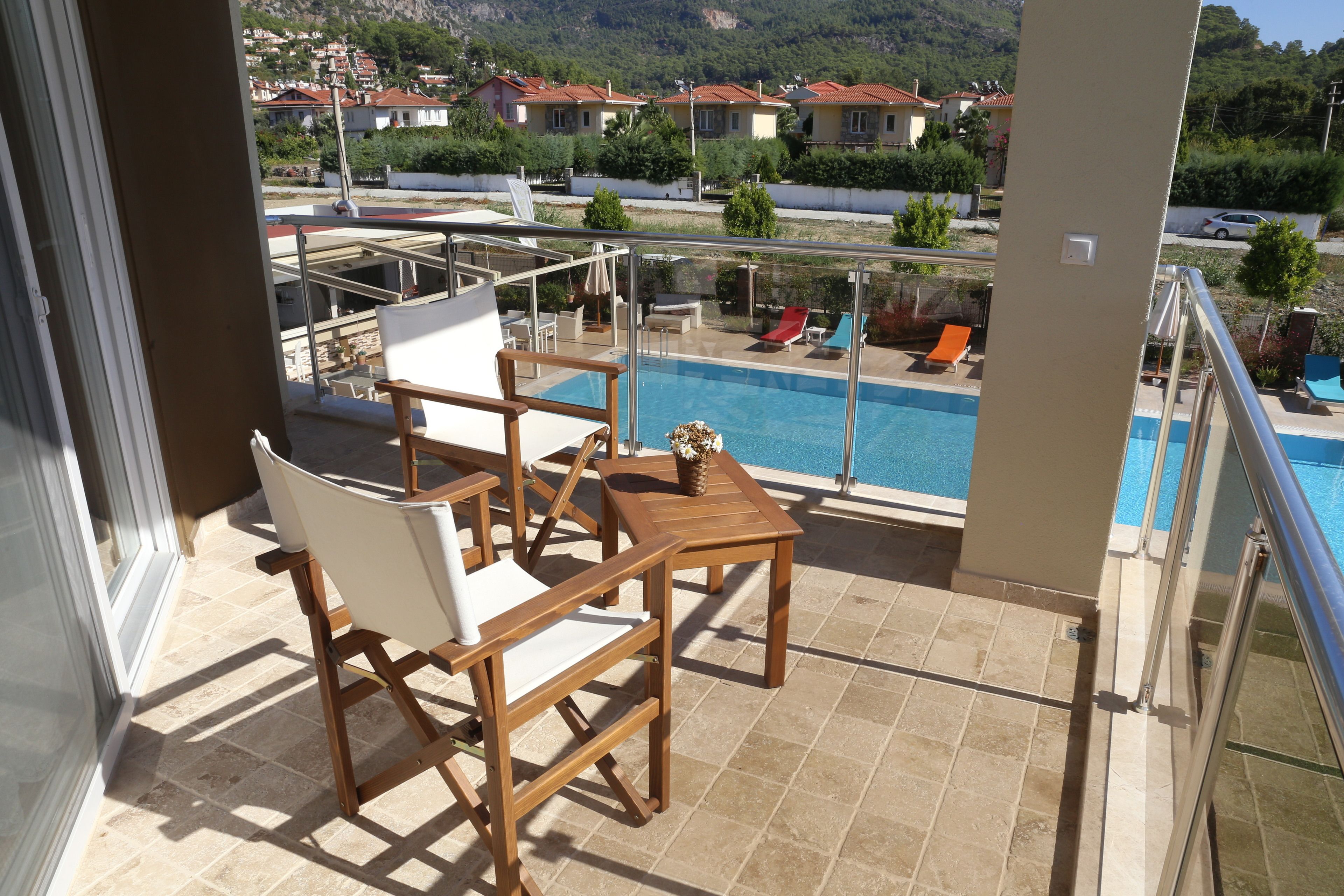Ein Balkon mit Pool, Holzmöbeln und Blick auf Häuser im Hintergrund.