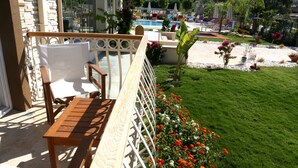 A balcony with wooden furniture, a pool, and a garden with flowers.