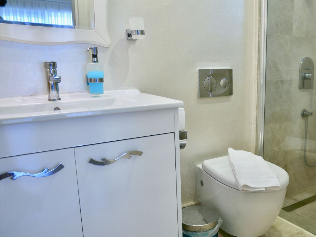 Un bany amb un lavabo blanc, un mirall, una dosificadora de sabó, un vàter i una zona de dutxa.