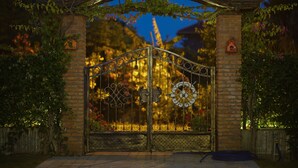 A wrought iron gate with intricate designs, flanked by brick pillars and adorned with flowering vines.