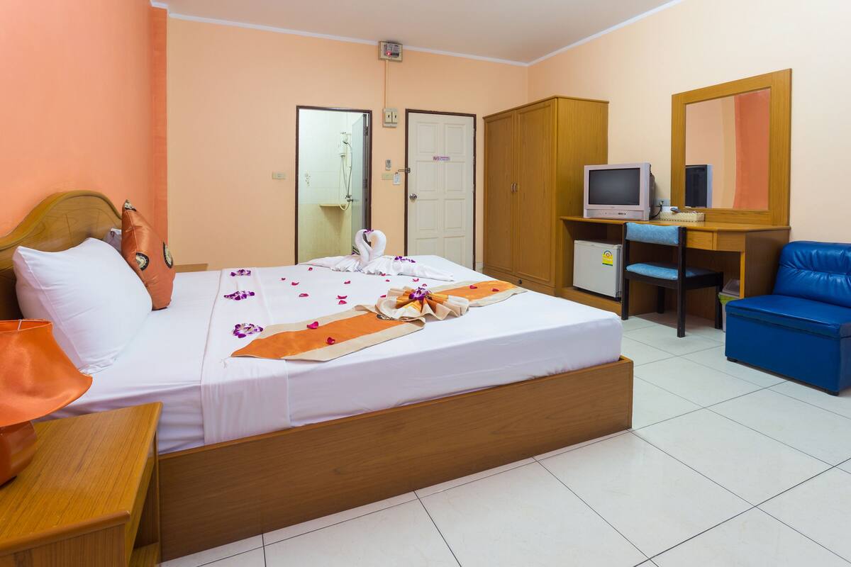A hotel room with a bed, a desk with a computer, a TV, a wardrobe, and a blue chair.
