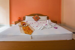 Un lit bien fait, avec un drap blanc, une tête de lit en bois et un seul oreiller orange.