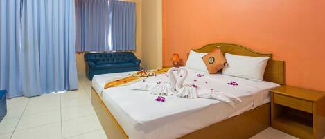 A hotel room with a bed, a nightstand, a blue sofa, and a window with curtains.