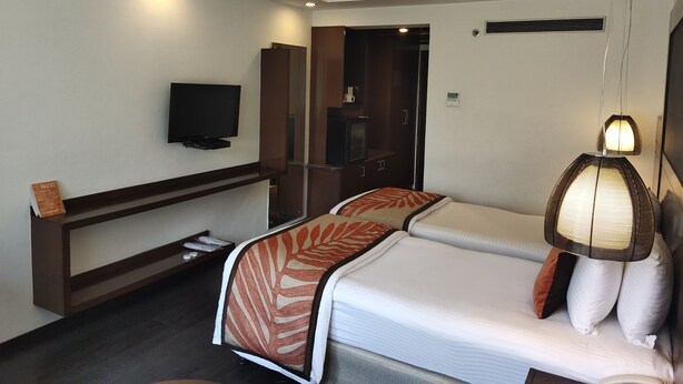 Habitación de hotel con cama, televisión montada en la pared, mesita de noche, armario y lámpara colgante.
