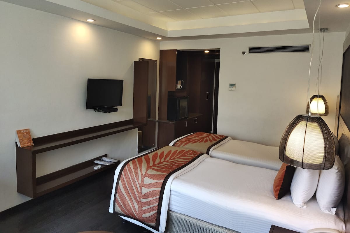 A hotel room with a bed, a TV mounted on the wall, a bedside table, a wardrobe, and a hanging light fixture.