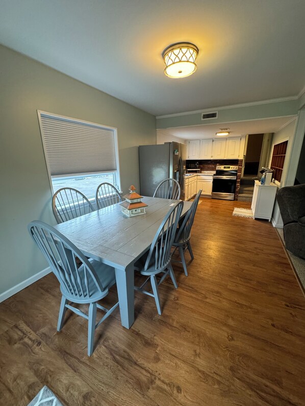 A dining area with a table and chairs, a kitchen in the background, and a ceiling light fixture. - Boulevard Motel (Marmora)