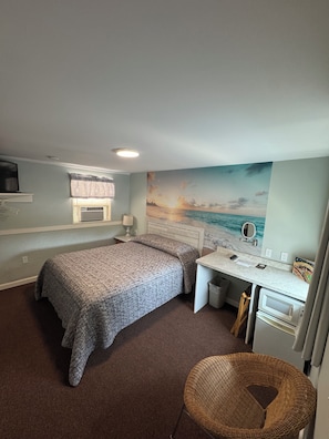 Un dormitorio con cama, escritorio, silla, televisor y un mural de playa.