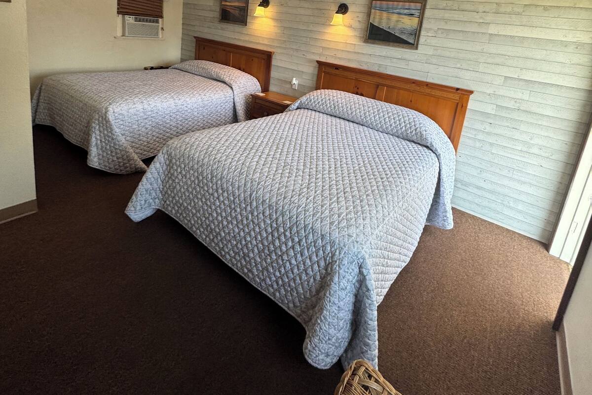 A hotel room with two beds, a wooden headboard, a wall-mounted air conditioner, and two wall-mounted lamps.