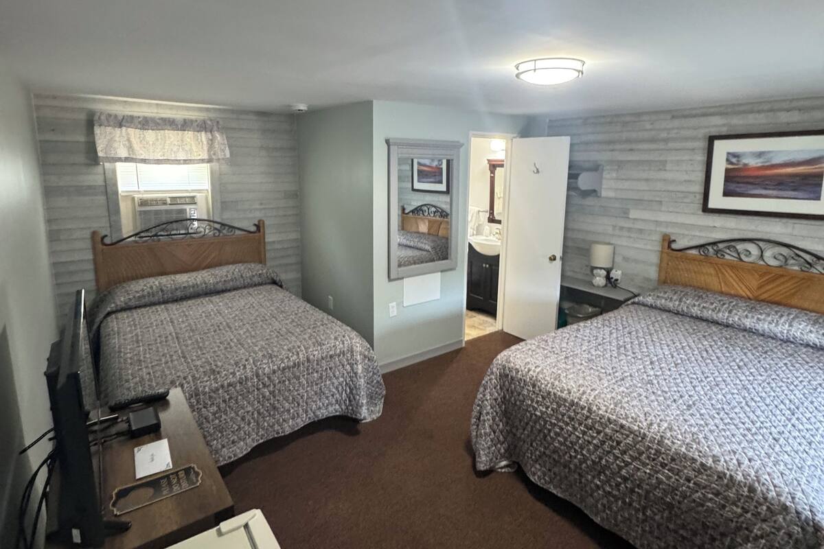 A hotel room with two beds, a desk with a computer, a TV, and a suitcase.