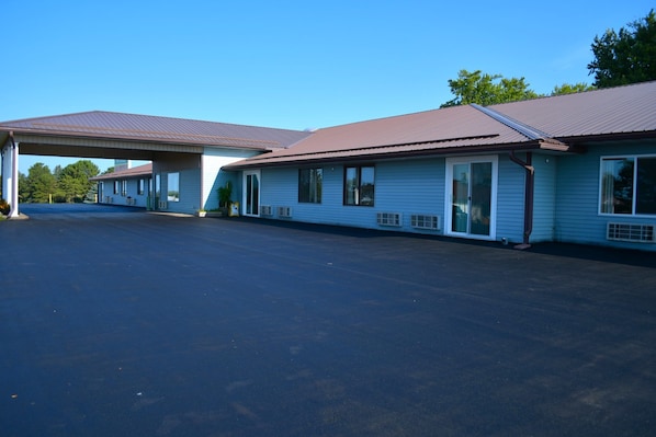 Un motel con estacionamiento techado y varias habitaciones con amplias ventanas.