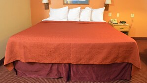 A hotel room with a large bed, two bedside lamps, a nightstand with a phone and clock, and a framed picture on the wall. - Old Towne Motel (Westby)
