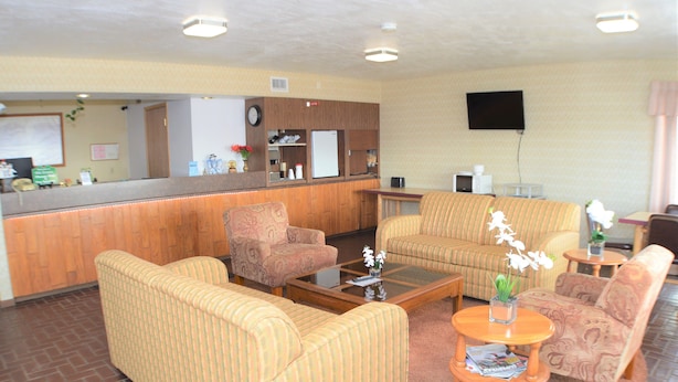 A hotel lobby with striped sofas, a wooden reception desk, a clock, and a flat-screen TV on the wall. - Old Towne Motel (Westby)