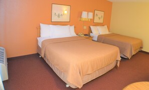 Two single beds with beige bedspreads and white pillows, complemented by wall-mounted lamps and framed prints.