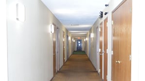A long, narrow hallway with carpeted floors and doors on both sides leading to individual rooms. - Old Towne Motel (Westby)