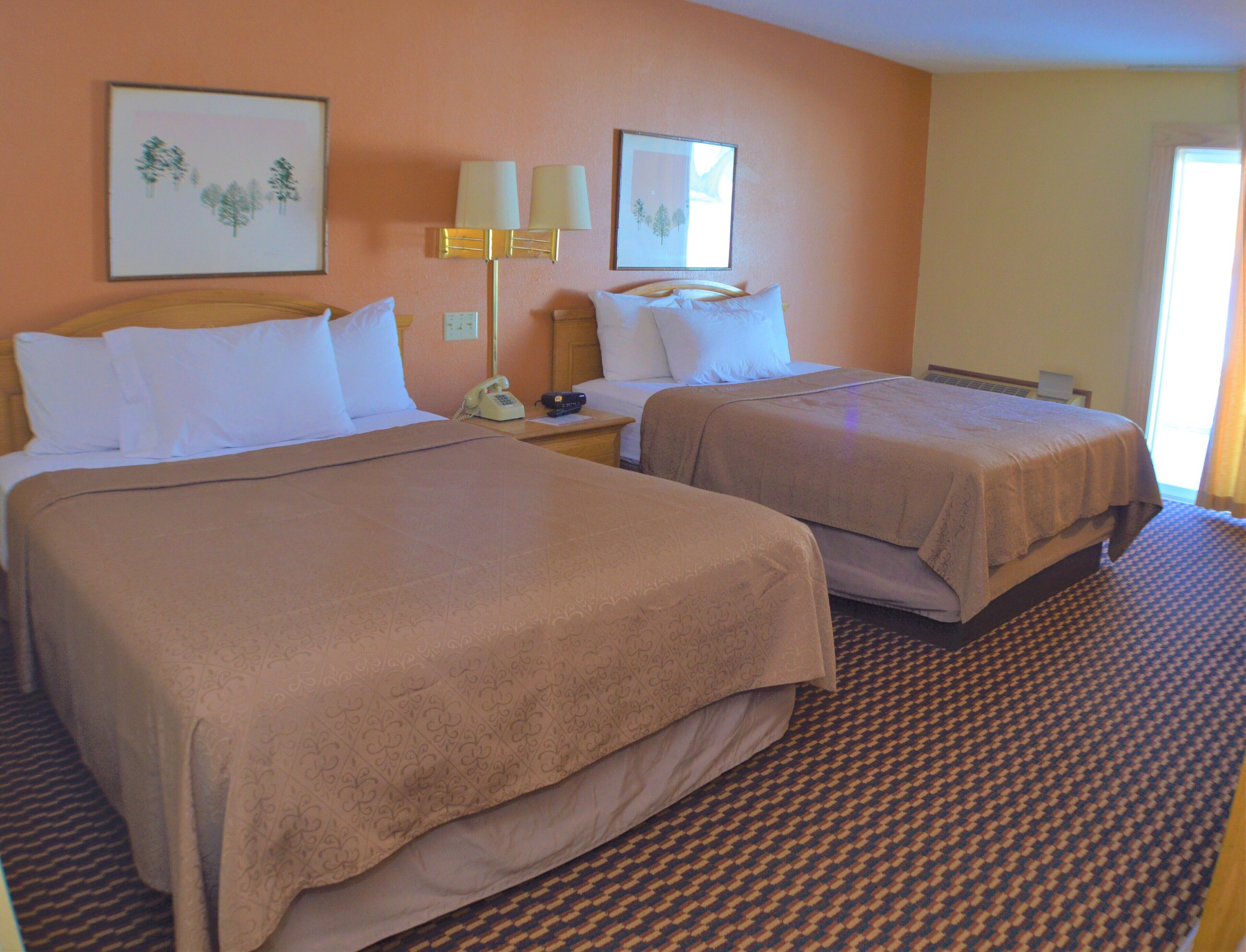 A hotel room with two beds, a telephone, and a lamp.