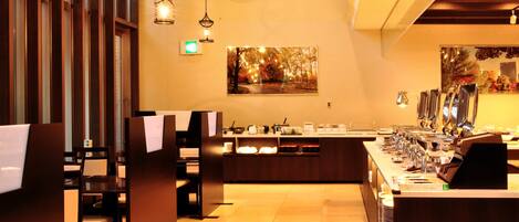 A restaurant with a long counter, multiple chairs, hanging lights, and a painting on the wall.