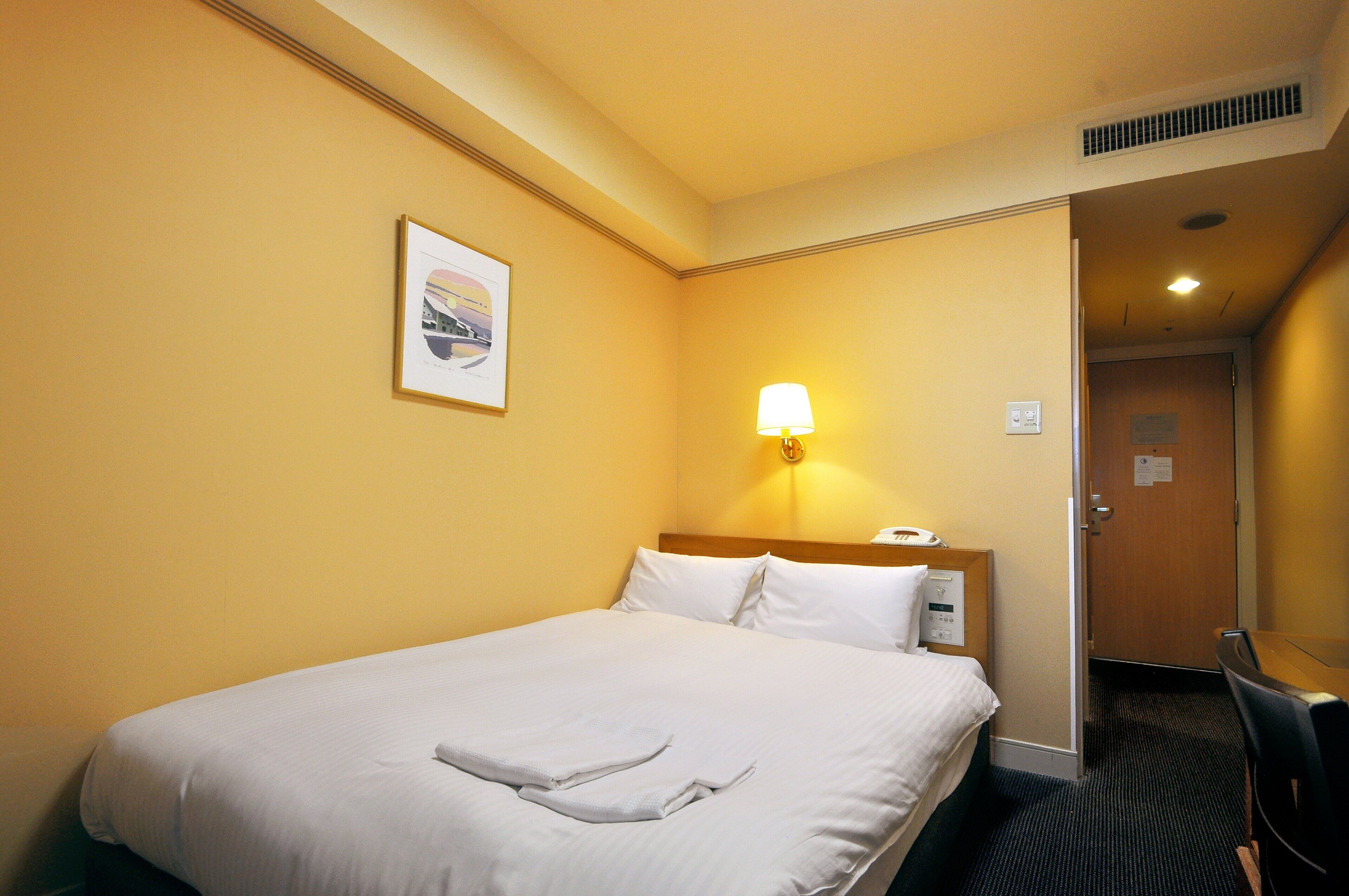 Et hotelværelse med seng, skrivebord, stol, lampe og dør.