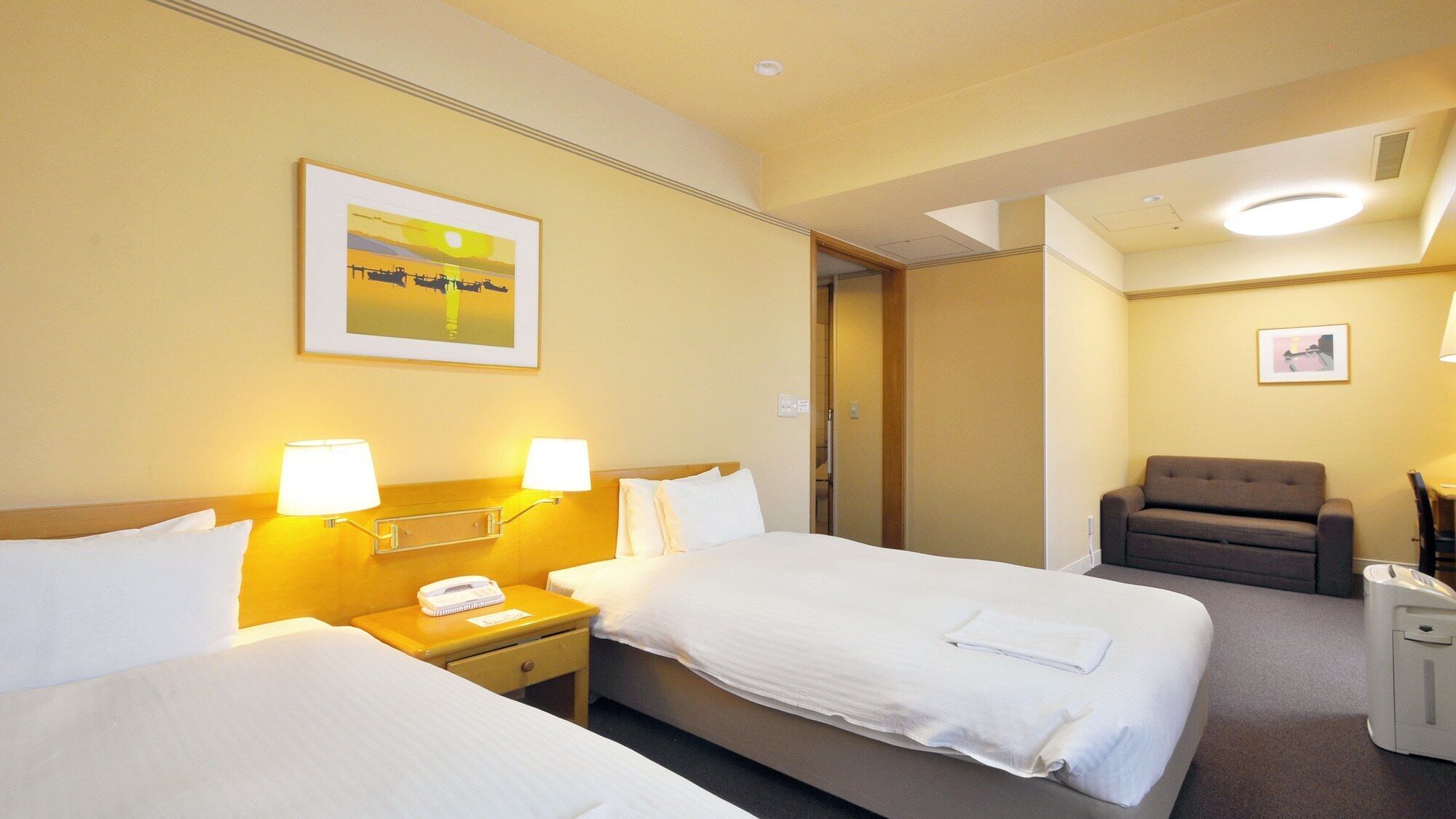 A hotel room with two beds, a chair, a desk with a lamp, and a painting on the wall.