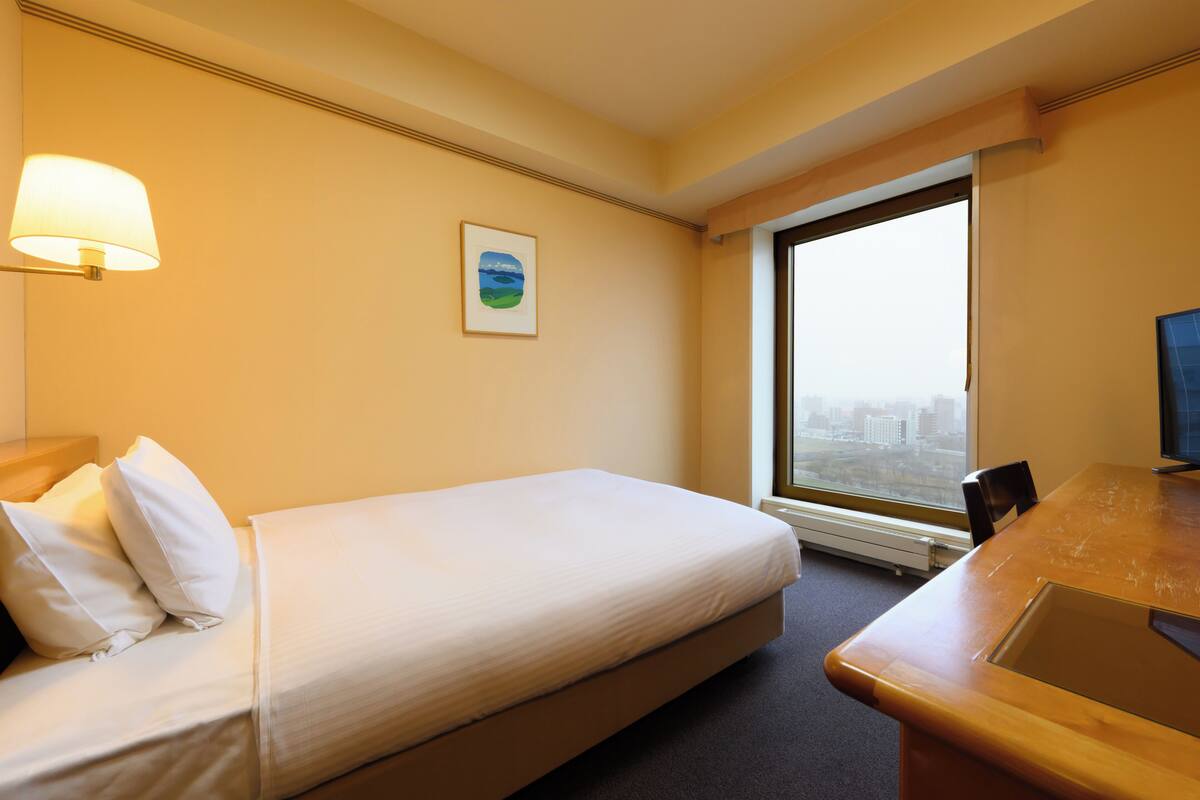 Habitación de hotel con cama, escritorio, silla, ventana y lámpara.