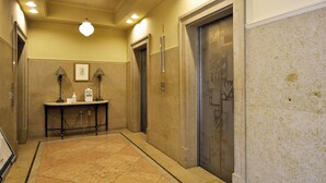 A hallway with an elevator, a reception desk with a phone and a small table, and a wall with a decorative panel. - Hotel Lifort Sapporo (Sapporo)
