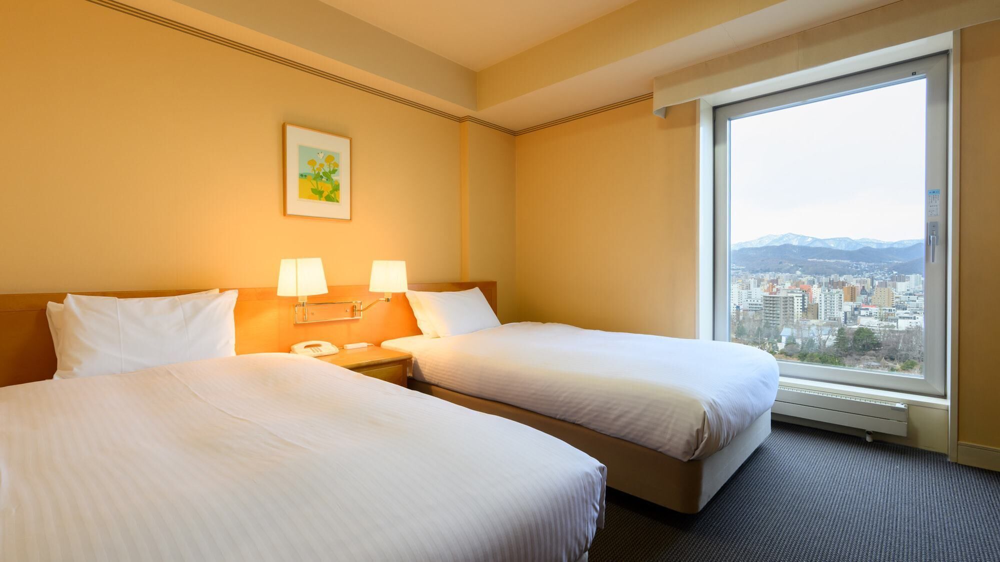 A hotel room with two beds, a bedside table with lamps, a phone, and a window with a city view.