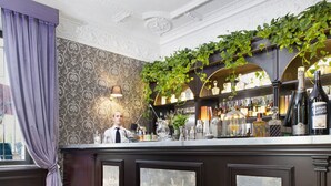 A bar area with a marble floor, a bartender, and a wall with framed artwork.