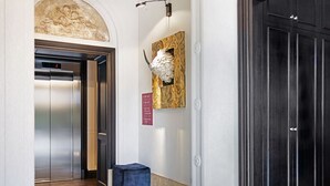 A marble-floored hallway with an elevator, a reception desk, and a dark wooden door.
