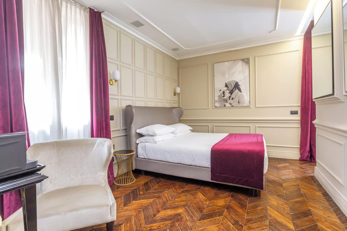 Une chambre d’hôtel avec un lit, une chaise, un bureau et un parquet à motifs en chevrons.