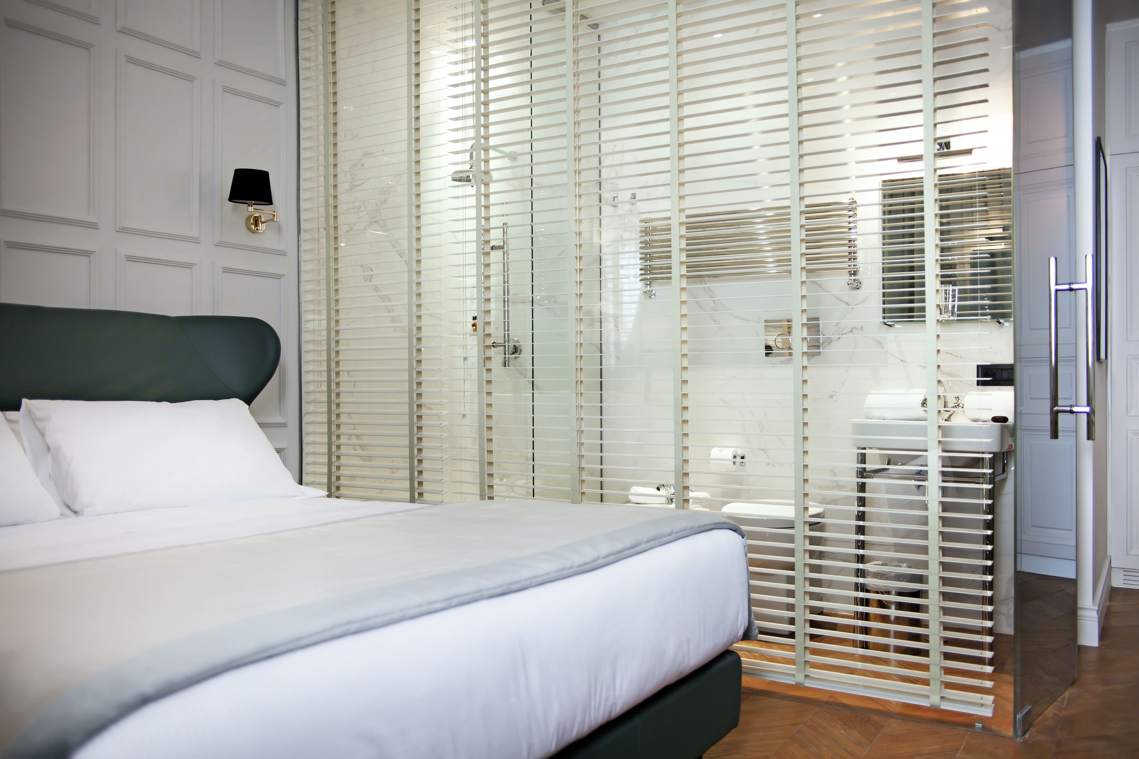 A bedroom with a bed, a nightstand, a wall-mounted lamp, and a sliding glass door leading to a bathroom.