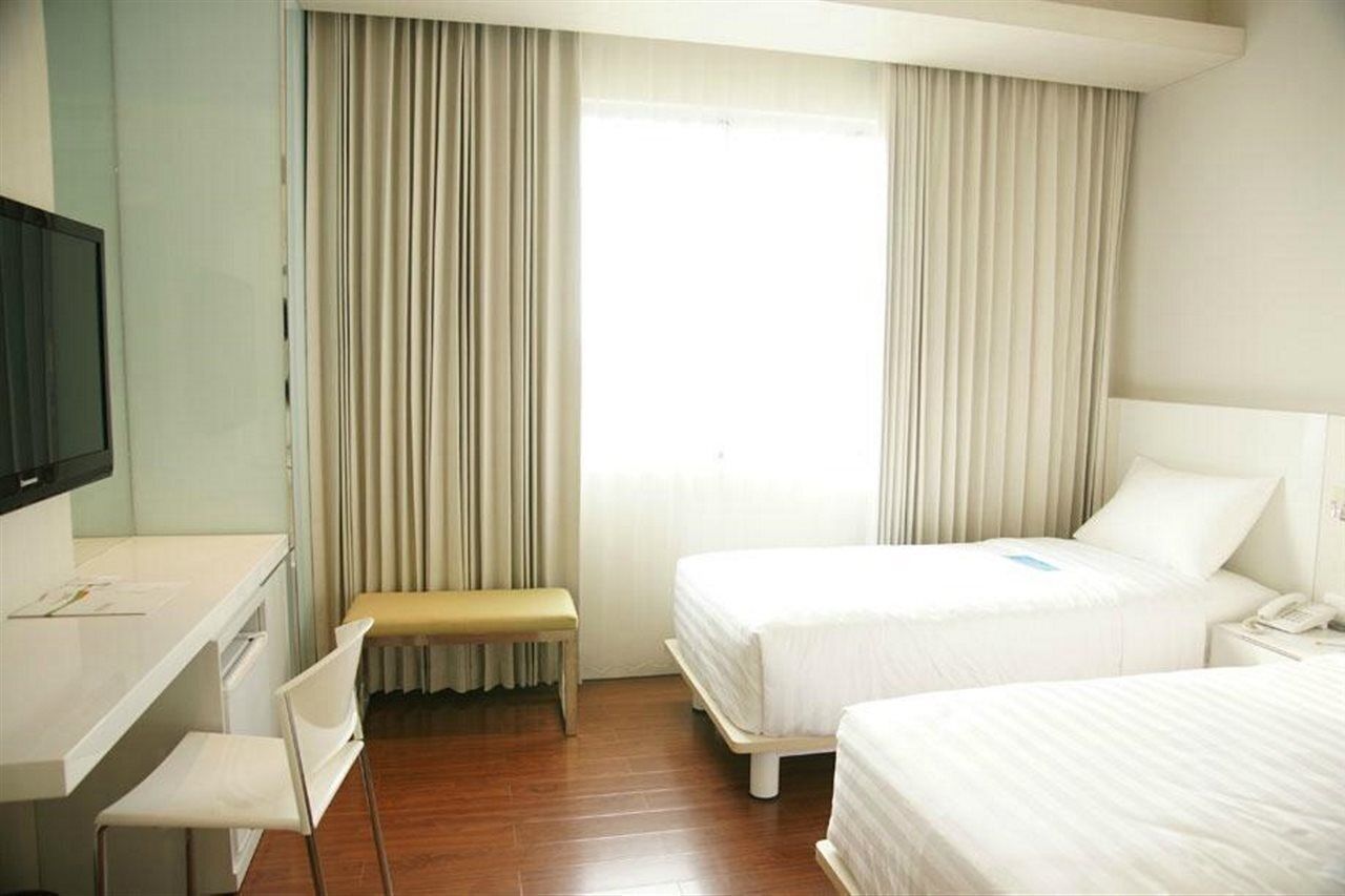 A hotel room with two beds, a desk, a chair, and a television.