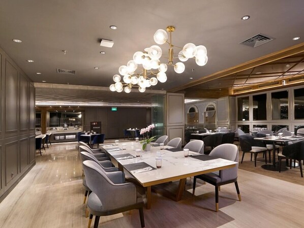 A modern dining area with a long table, multiple chairs, and a central chandelier. - Everbright (Surabaya)