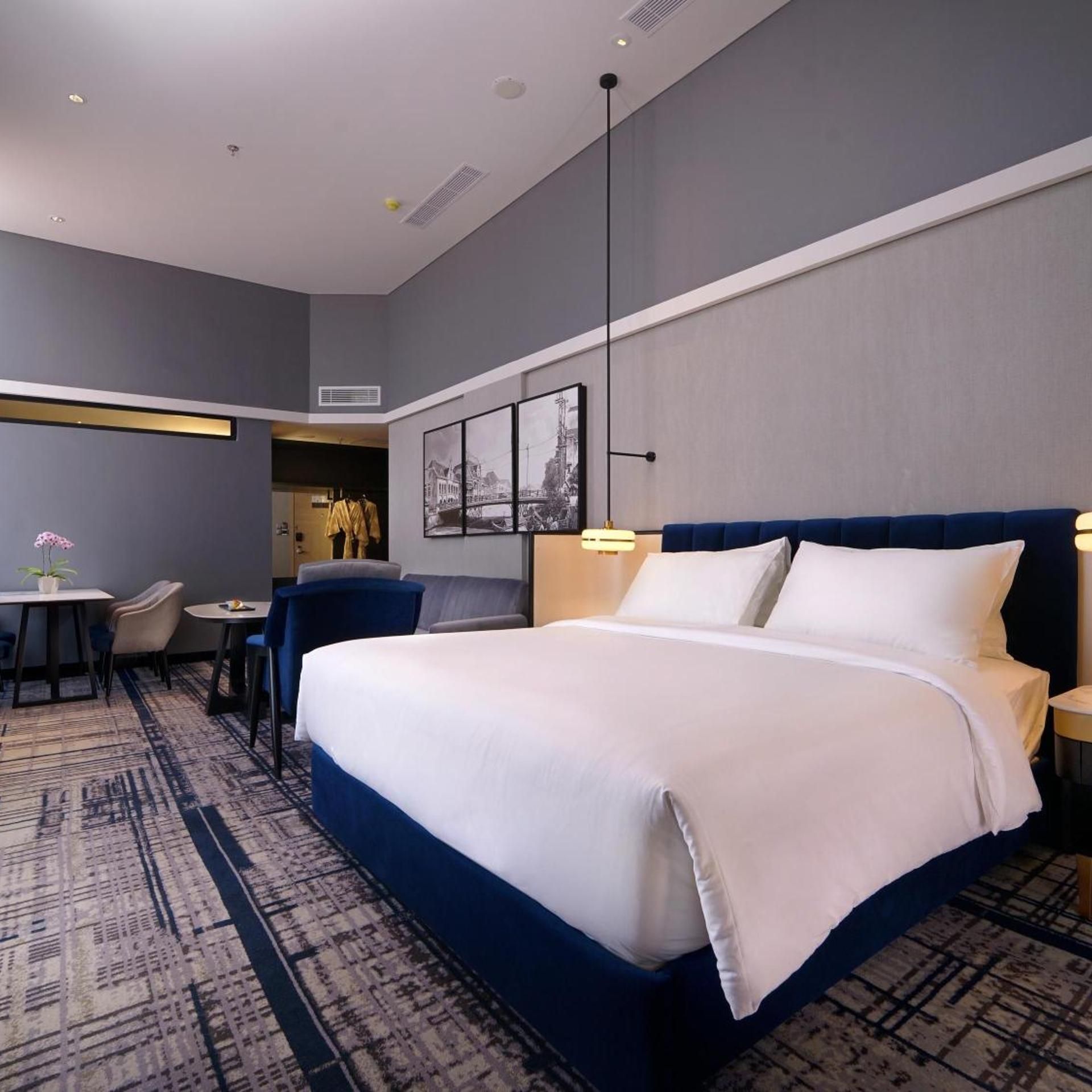 A hotel room with a large bed, a desk, a chair, and a small table with a plant.