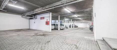 A parking garage with multiple parking spaces, concrete floors, and overhead lighting.