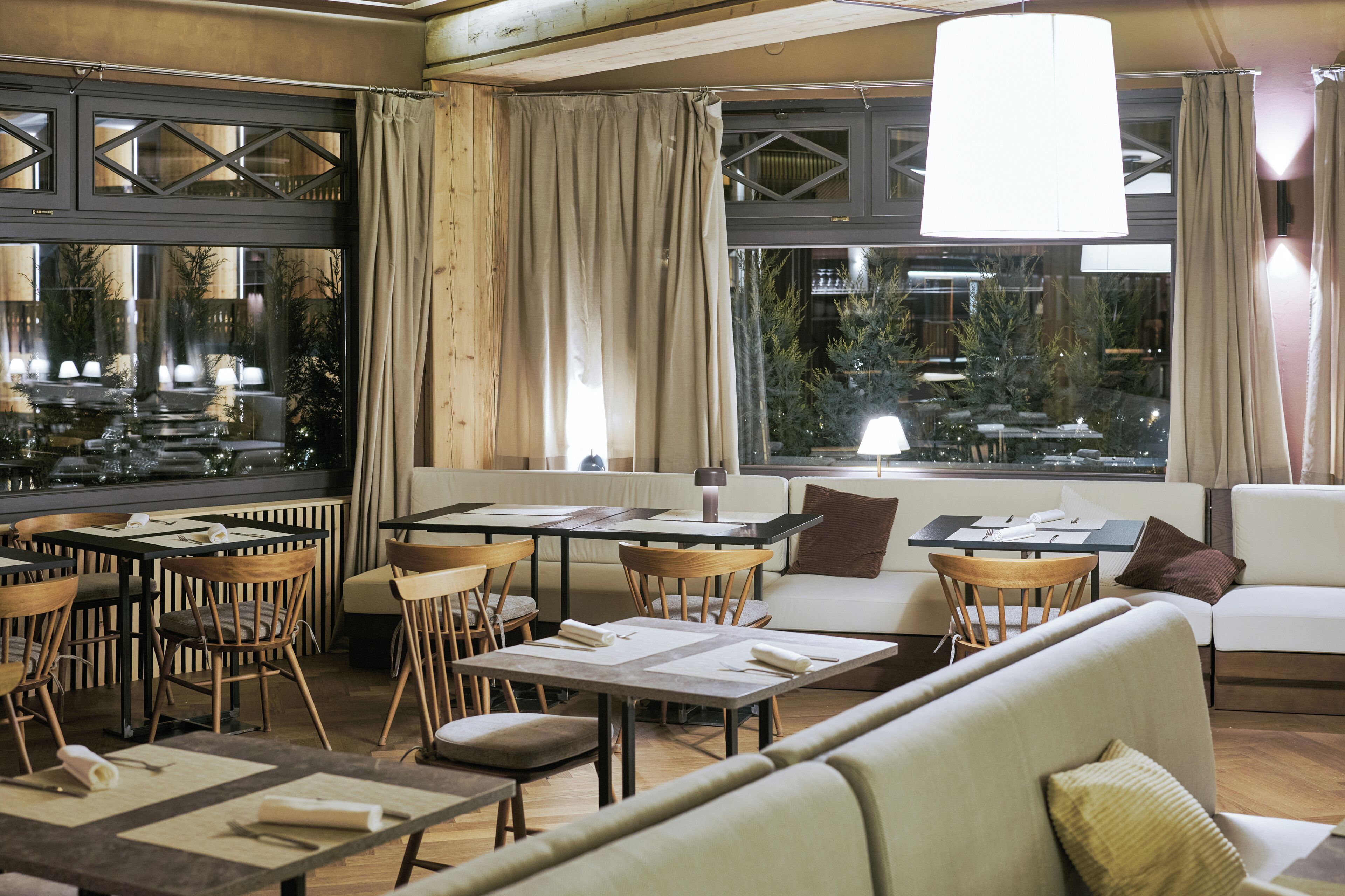 Un restaurant avec des tables et des chaises, un canapé et une grande fenêtre avec des rideaux.