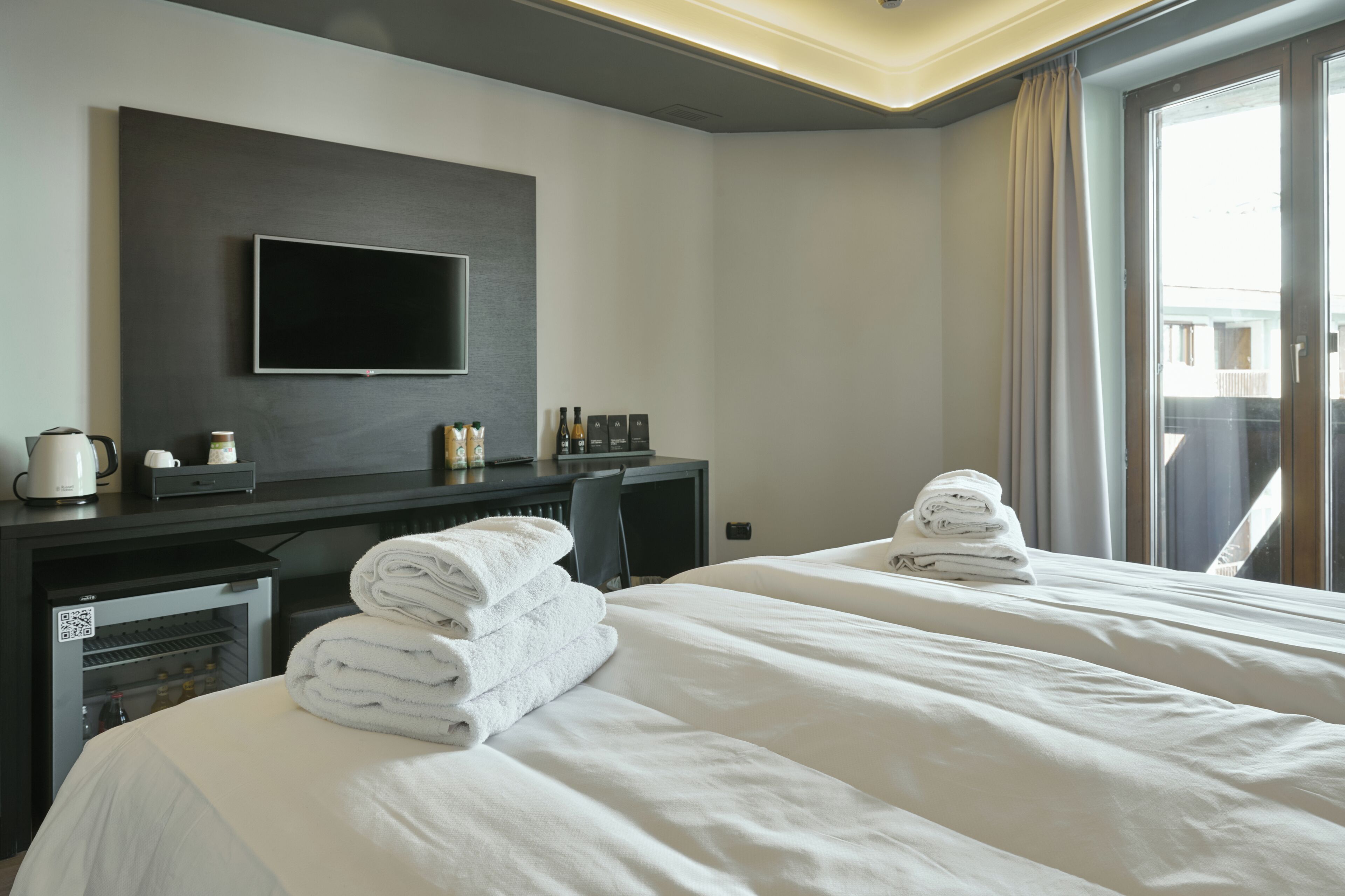 Camera d'albergo con due letti, una TV a schermo piatto montata a parete, una scrivania con macchina del caffè e un minibar.